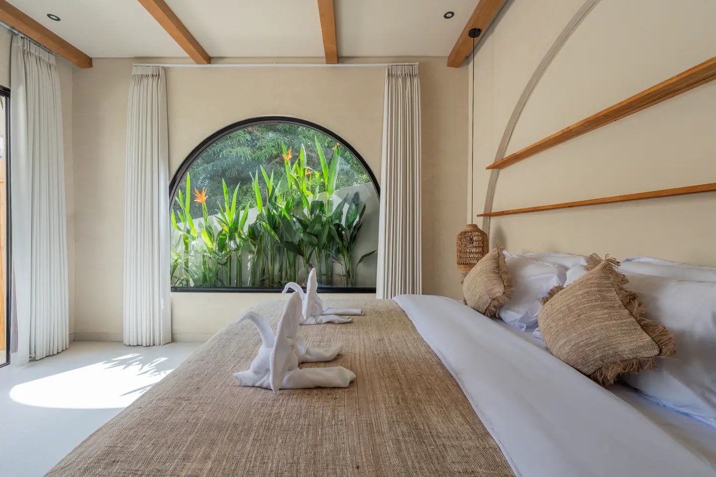 Calm bedroom framed by a curved window and tropical greenery